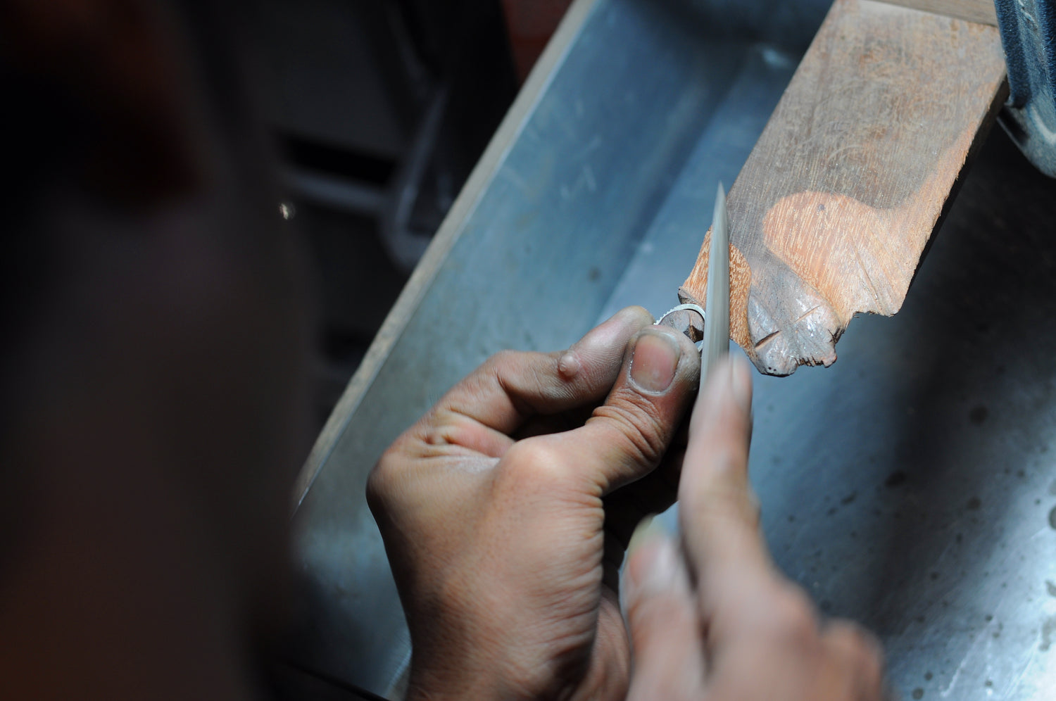 Jeweler’s hands carefully filing a sterling silver ring on a wooden bench pin during finishing process.
