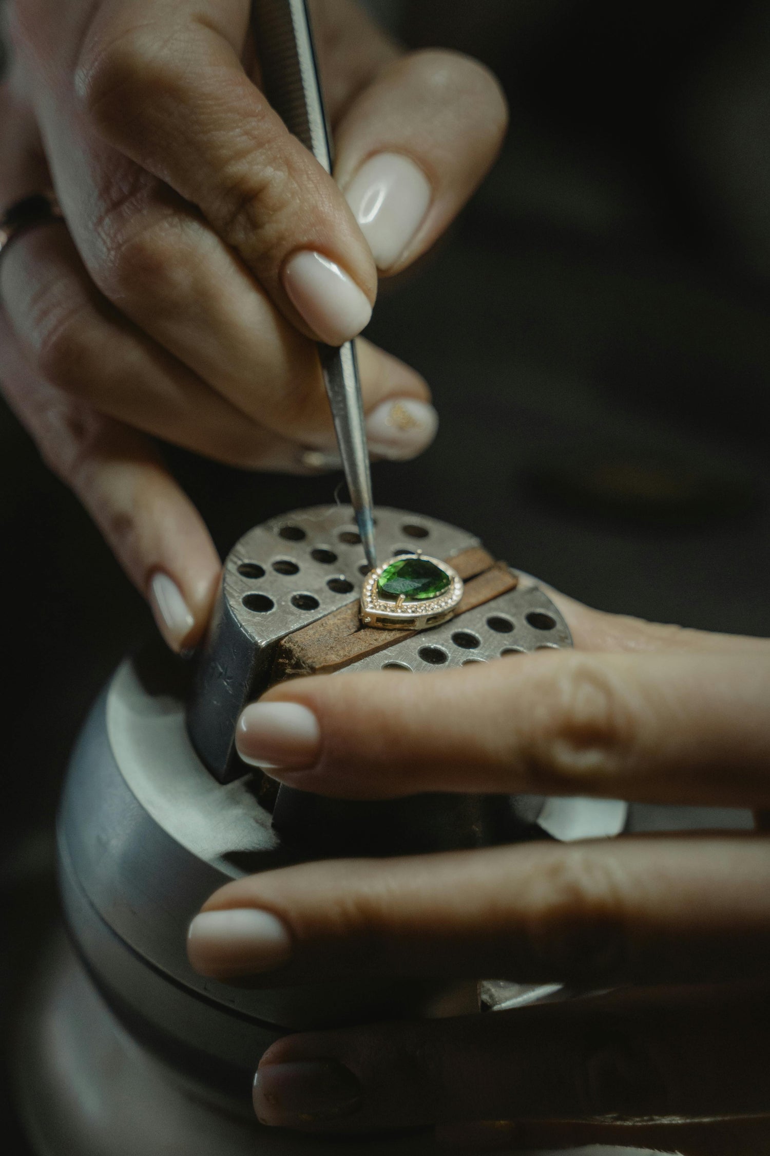 Jeweler hand-setting a green gemstone on a gold ring in a precision vise